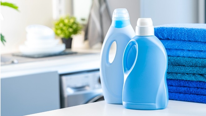 twee wasmiddelen met blauwe verpakking staan op een wasmachine naast een paar blauwe handdoeken